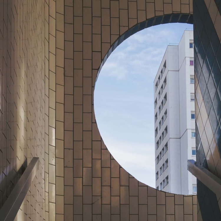 Round window in a stairwell looking out to blue skies.